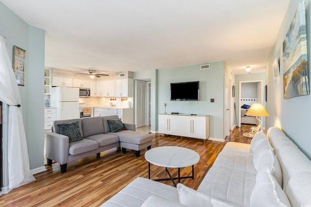 living room featuring light wood-style floors, a ceiling fan, and baseboards