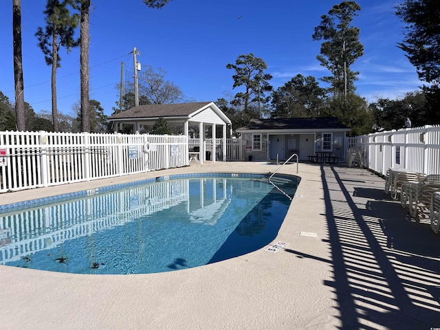 community pool with a patio area, fence, and an outbuilding