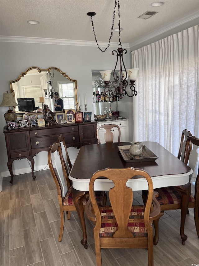 dining space featuring visible vents, ornamental molding, a textured ceiling, and wood finish floors