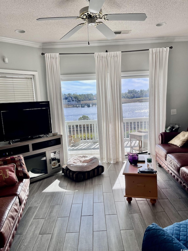 living area with a water view, ornamental molding, a textured ceiling, and ceiling fan