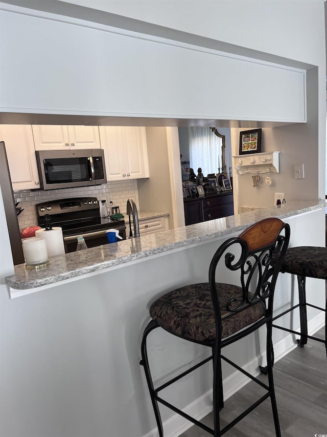 kitchen with a kitchen bar, appliances with stainless steel finishes, tasteful backsplash, light stone counters, and a peninsula