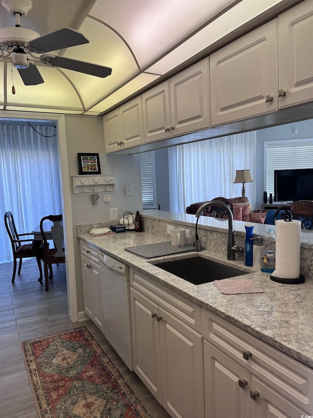 kitchen with a ceiling fan, dishwasher, a sink, light stone counters, and white cabinets
