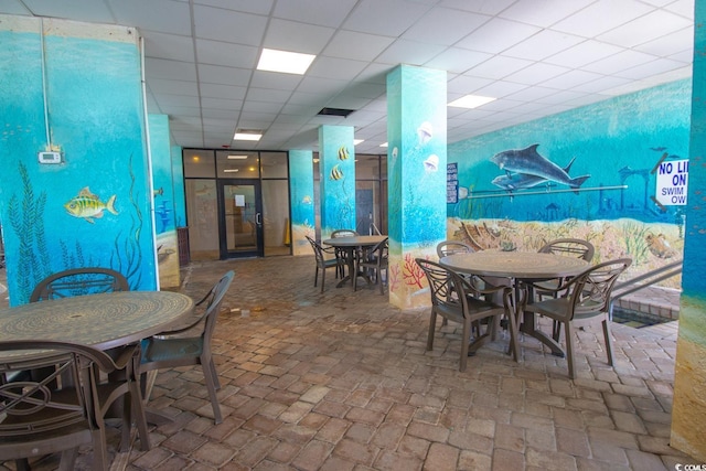 dining room featuring a drop ceiling and brick floor