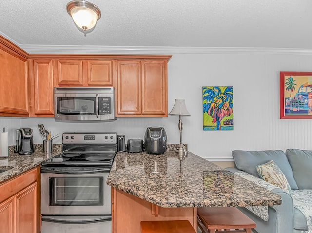 4516 Seaview St Unit 135, North Myrtle Beach, SC 29582 - kitchen featuring appliances with stainless steel finishes, a kitchen breakfast bar, crown molding, dark stone counters, and brown cabinetry