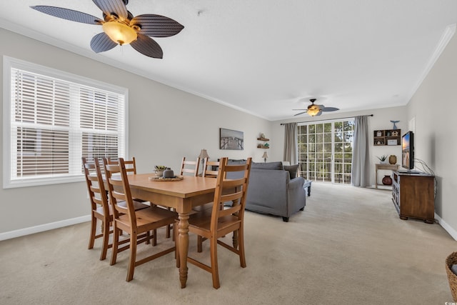 dining room featuring light colored carpet, ornamental molding, baseboards, and a ceiling fan