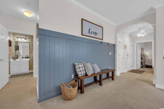 hallway featuring arched walkways, baseboards, ornamental molding, light carpet, and light tile patterned flooring