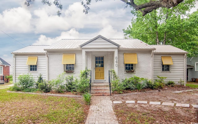 bungalow-style home with metal roof, brick siding, and entry steps