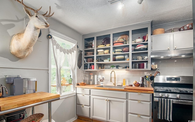 kitchen with stainless steel gas range, under cabinet range hood, a sink, wooden counters, and a textured ceiling