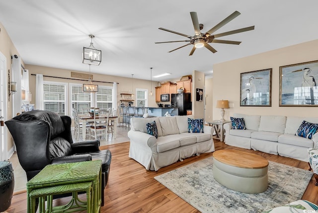 living room with light wood finished floors and ceiling fan with notable chandelier