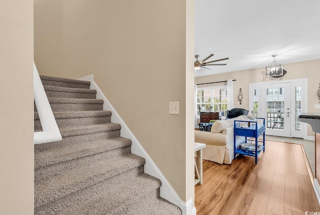 stairway featuring baseboards, ceiling fan with notable chandelier, and wood finished floors