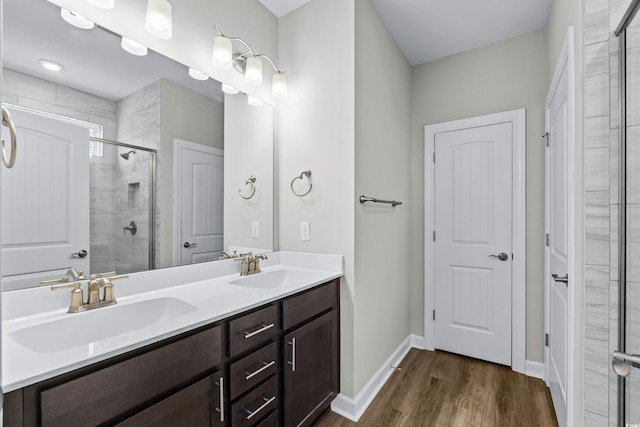 full bath featuring wood finished floors, double vanity, a sink, and a stall shower