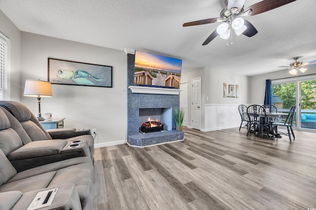 living room with a fireplace, a textured ceiling, a ceiling fan, baseboards, and wood finished floors