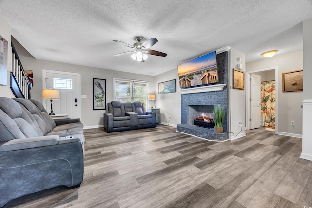 living room featuring a brick fireplace, a ceiling fan, a textured ceiling, and wood finished floors