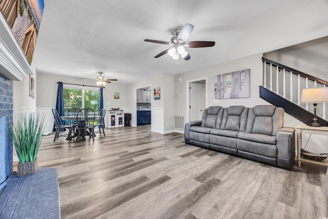 living room with visible vents, wood finished floors, a fireplace, stairway, and a ceiling fan