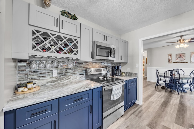 kitchen featuring light wood-type flooring, a ceiling fan, appliances with stainless steel finishes, and blue cabinets