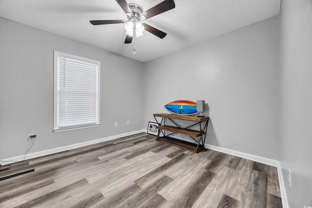 spare room with a textured ceiling, baseboards, a ceiling fan, and wood finished floors