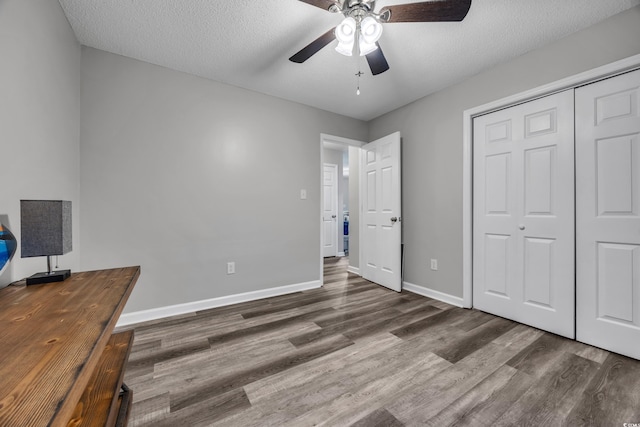 unfurnished bedroom featuring a textured ceiling, a ceiling fan, baseboards, wood finished floors, and a closet
