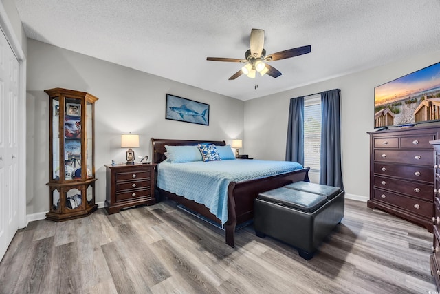 bedroom featuring a ceiling fan, a textured ceiling, wood finished floors, baseboards, and a closet