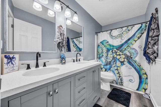 bathroom featuring double vanity, toilet, a sink, and wood finished floors
