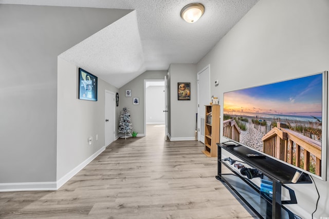 hallway with baseboards, a textured ceiling, wood finished floors, and vaulted ceiling