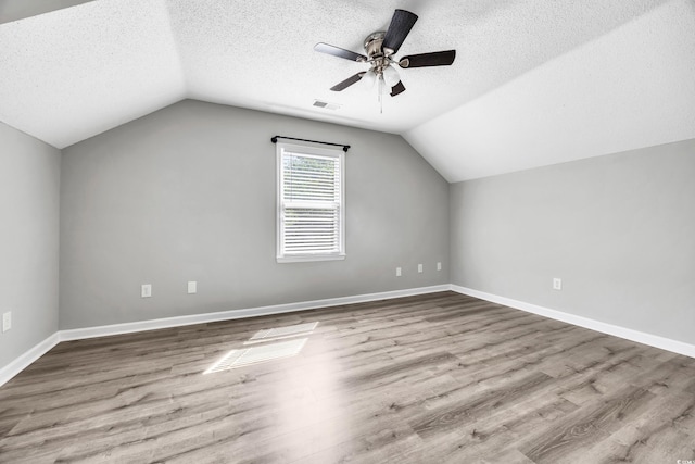 additional living space with ceiling fan, a textured ceiling, wood finished floors, vaulted ceiling, and visible vents