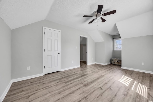 additional living space with wood finished floors, baseboards, ceiling fan, a textured ceiling, and vaulted ceiling