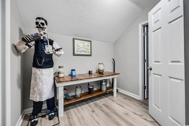 foyer entrance featuring baseboards, a textured ceiling, light wood-style flooring, and lofted ceiling