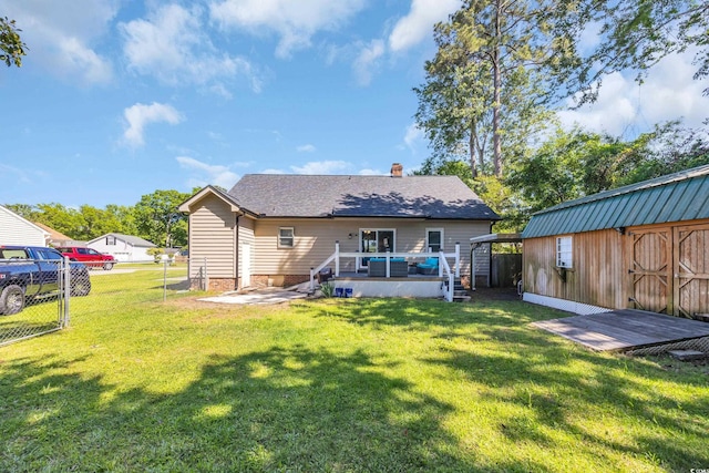 back of property featuring an outdoor structure, fence, a deck, a chimney, and a lawn
