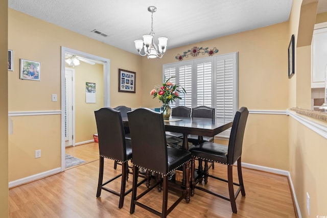 dining space featuring baseboards, visible vents, light wood finished floors, and ceiling fan with notable chandelier