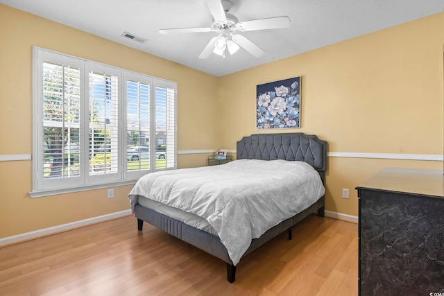 bedroom with a ceiling fan, baseboards, visible vents, and wood finished floors