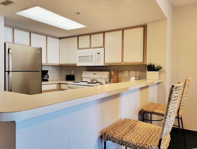 kitchen featuring a textured ceiling, visible vents, light countertops, a peninsula, and white appliances