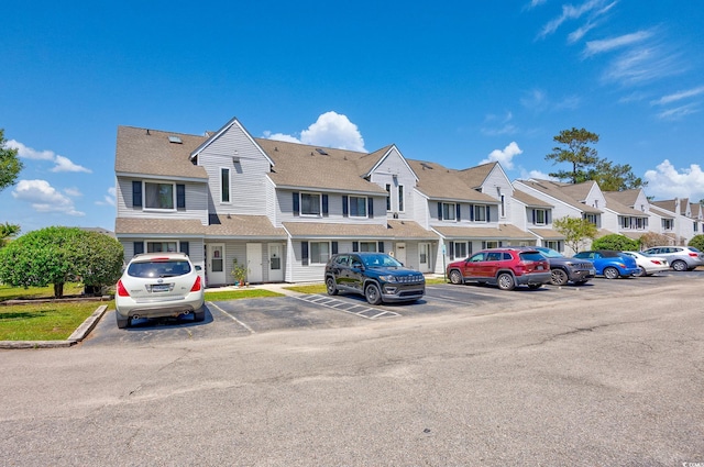 view of front of property featuring a residential view, uncovered parking, and a shingled roof
