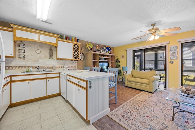 kitchen with a sink, a peninsula, dishwasher, a textured ceiling, and light countertops