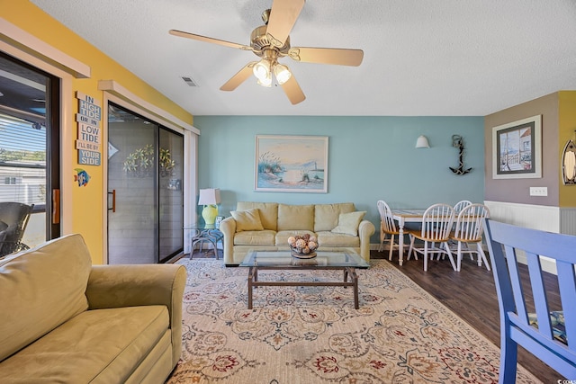 living room with a textured ceiling, wood finished floors, a ceiling fan, and wainscoting