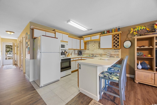 kitchen with white appliances, a peninsula, light countertops, decorative backsplash, and a sink