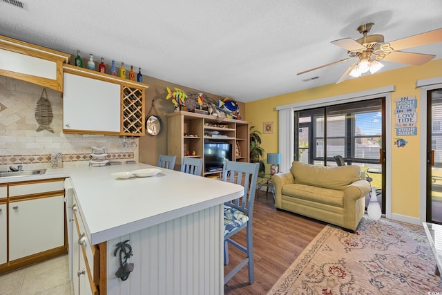 kitchen featuring a peninsula, light countertops, a kitchen bar, backsplash, and a textured ceiling