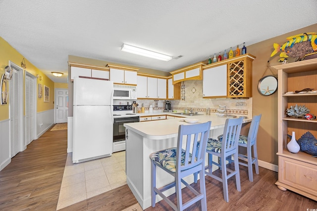 kitchen with white appliances, a peninsula, light countertops, backsplash, and a sink
