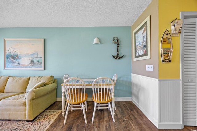 dining room featuring a textured ceiling, wood finished floors, and a wainscoted wall