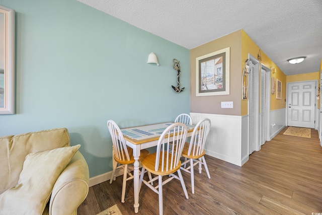 dining room featuring a textured ceiling, wood finished floors, and wainscoting