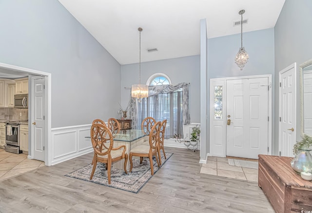 dining space with high vaulted ceiling, a notable chandelier, visible vents, and light wood-style floors
