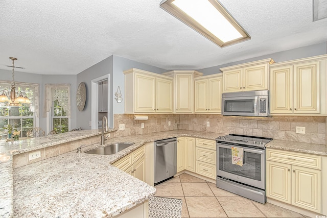 kitchen with light stone counters, a sink, stainless steel appliances, cream cabinetry, and backsplash