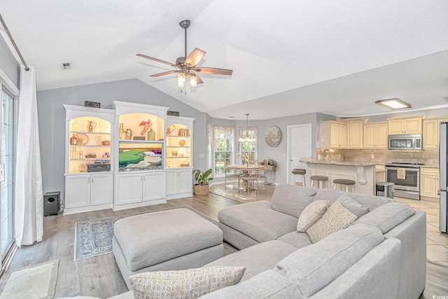 living area featuring light wood-style floors, ceiling fan, visible vents, and lofted ceiling