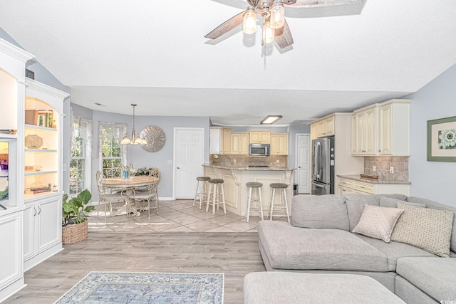 living room with lofted ceiling, ceiling fan with notable chandelier, and light wood-style floors