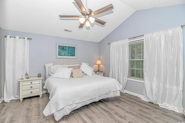 bedroom featuring visible vents, light wood-style floors, baseboards, a ceiling fan, and vaulted ceiling