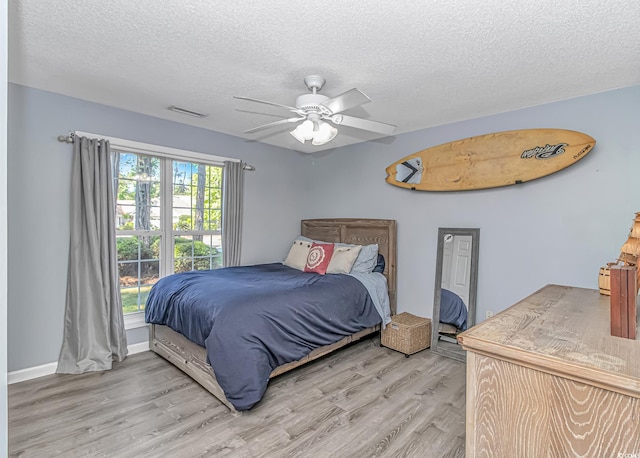 bedroom featuring visible vents, baseboards, a textured ceiling, a ceiling fan, and light wood-style flooring