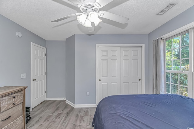 bedroom featuring a textured ceiling, light wood-style flooring, baseboards, visible vents, and a closet