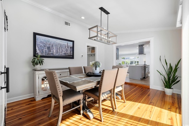 dining area featuring visible vents, baseboards, wood-type flooring, an inviting chandelier, and ornamental molding