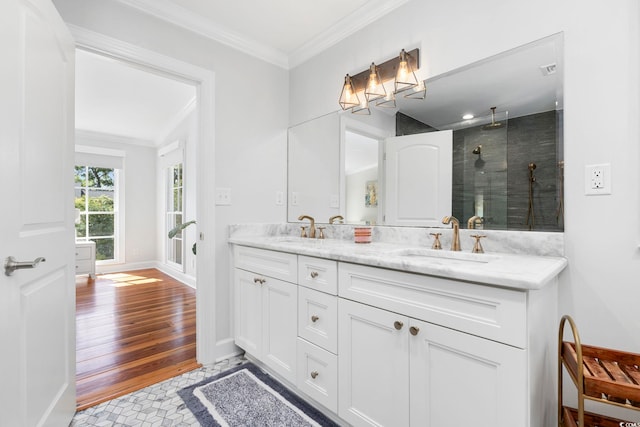 full bathroom with crown molding, a sink, a tile shower, and double vanity