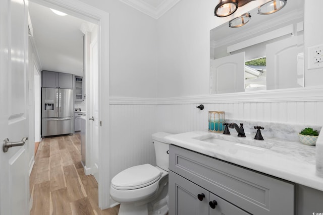 half bathroom with crown molding, wainscoting, vanity, toilet, and wood finished floors