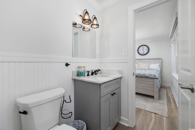 ensuite bathroom with crown molding, wainscoting, wood finished floors, toilet, and ensuite bathroom